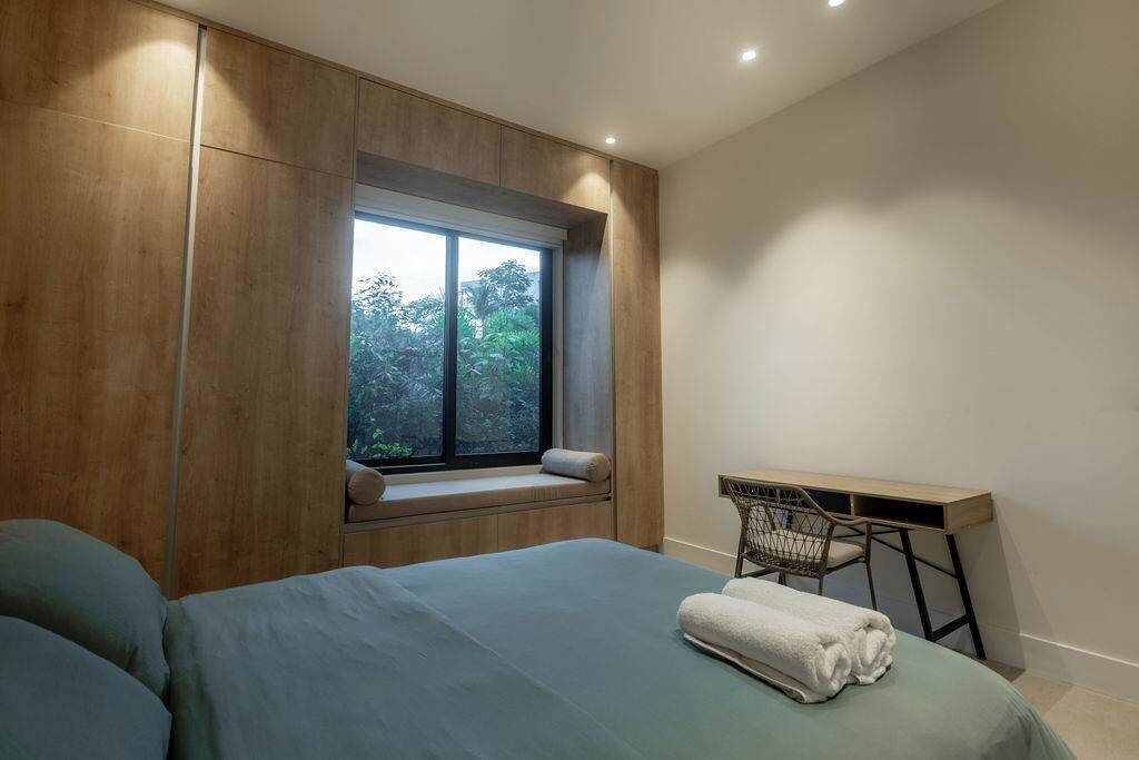 A bedroom with a large bed, a window with a view of trees, a desk, and a chair.