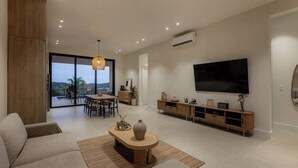 A modern living room with a sofa, coffee table, TV, and a dining area with a table and chairs. - Hillside Oceanview Home with Pool in Venao (Playa Venao)