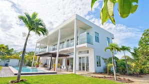 Een modern huis met twee verdiepingen, met zwembad, omringd door palmbomen en een verzorgd gazon.