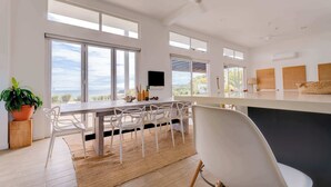 Een moderne keuken met grote ramen, een eethoek met witte stoelen en uitzicht op de oceaan.