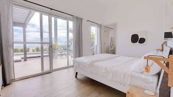 A modern bedroom with a large sliding glass door leading to an outdoor area, a bed with white bedding, and a wooden nightstand.