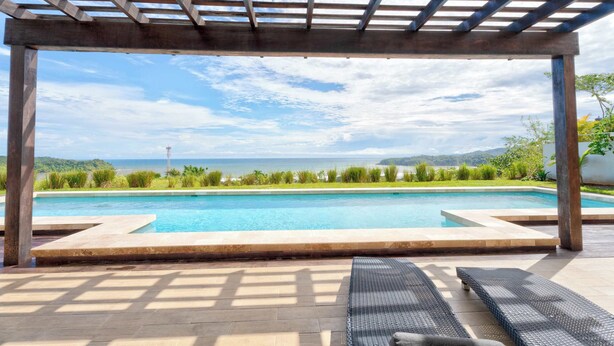 Een zwembadgedeelte met een pergola, ligbedden en uitzicht op de oceaan.