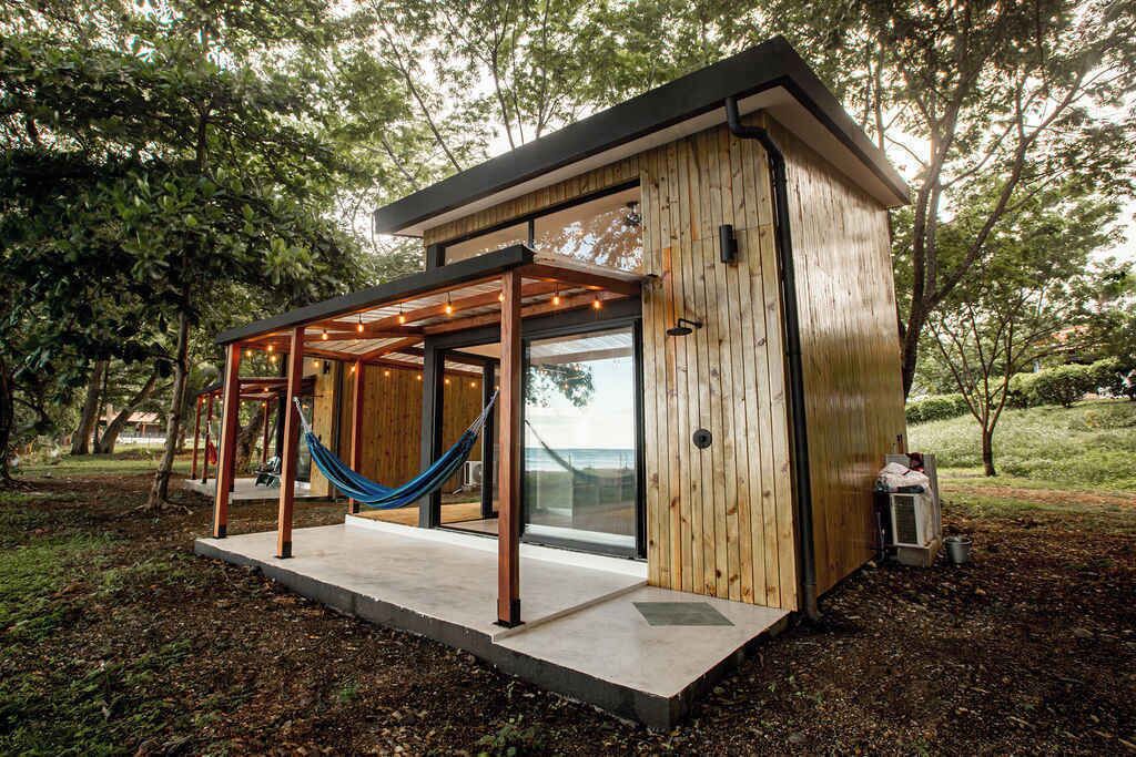 Eine moderne Holzhütte mit Glastür, einer Hängematte und einer Betonterrasse.