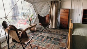 Ein Zeltraum mit einem Bett, einer Holzkommode, einem Tisch mit Stühlen und einem gemusterten Teppich.