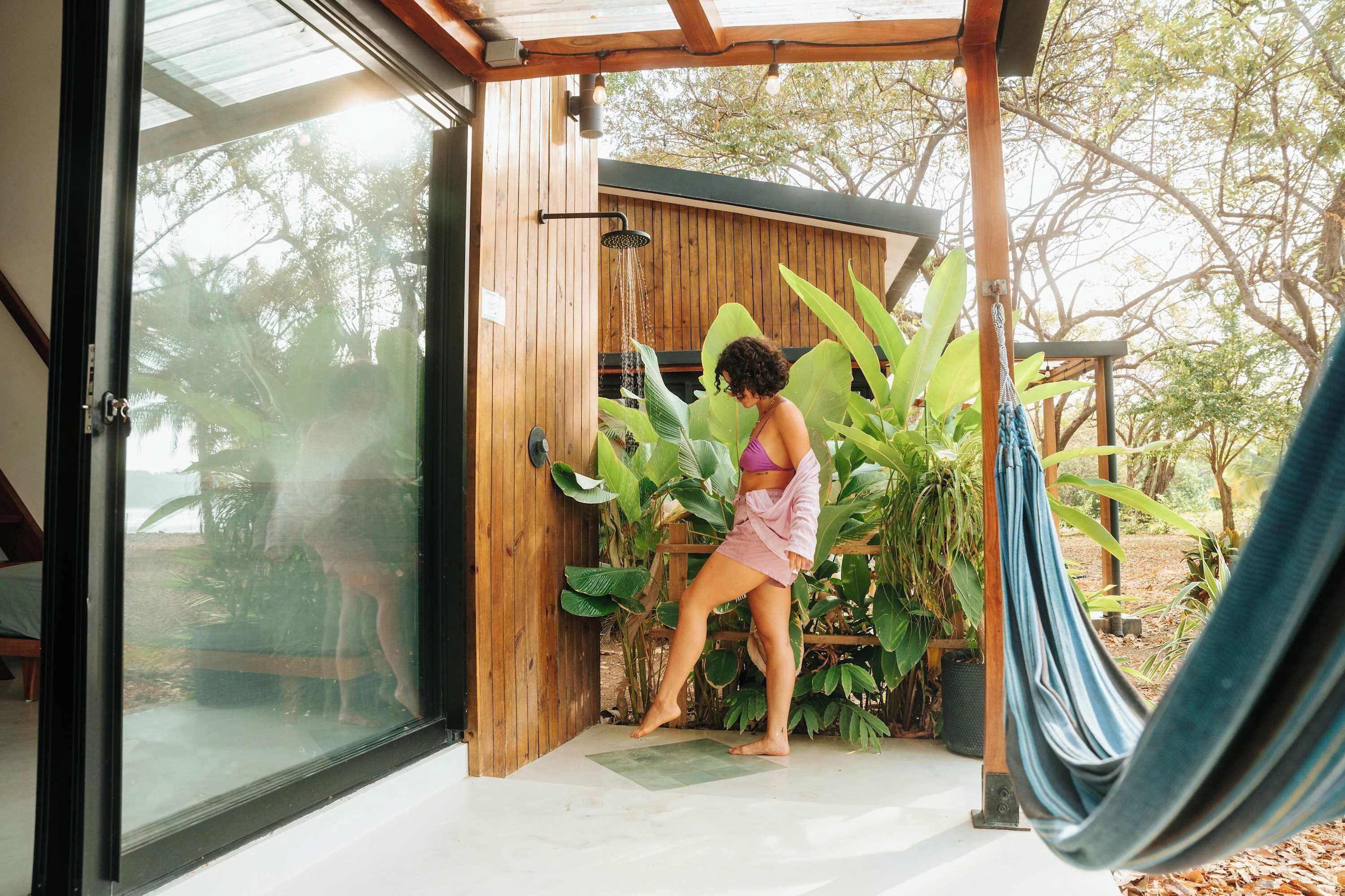 A wooden structure with a glass door, a hammock, and large green plants.