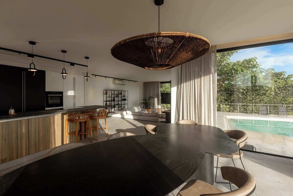 A modern kitchen with a dining area, a large dining table, and a view of a swimming pool.