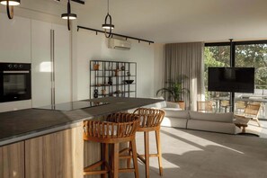 Una cocina moderna con una isla central, taburetes de bar, horno empotrado y televisión en la sala de estar.