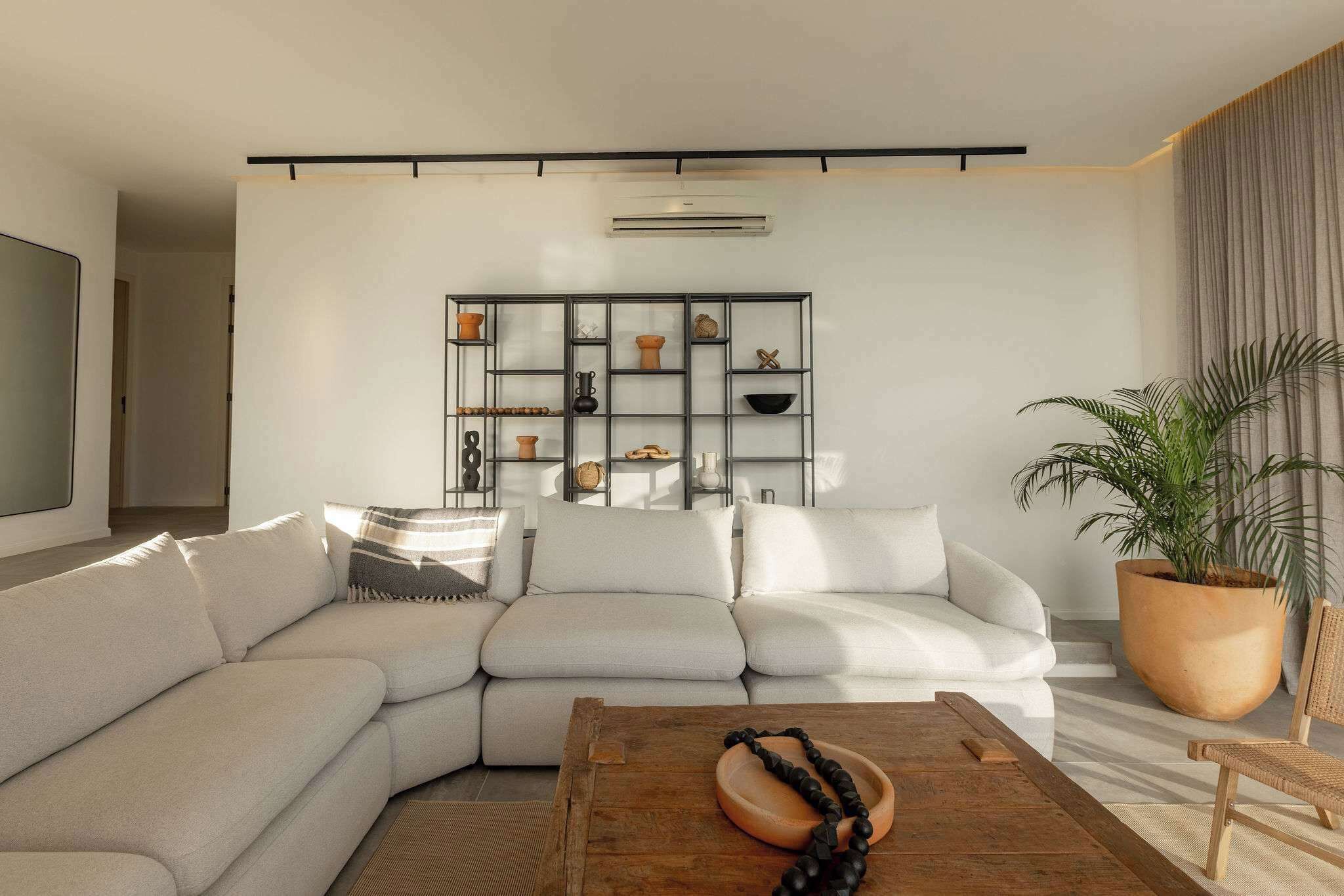 A modern living room with a sectional sofa, a wooden coffee table, and a decorative shelf with various items.