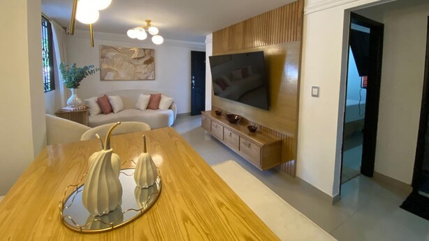 Un salon moderne avec une table à manger en bois, un téléviseur à écran plat fixé au mur et un canapé à l’arrière-plan.