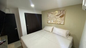 Une chambre à coucher avec un grand lit, une porte sombre, un mur de couleur claire et un luminaire au plafond.