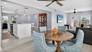 Een moderne keuken met witte kasten, een centraal eiland en een eethoek met een ronde tafel en blauwe beklede stoelen.