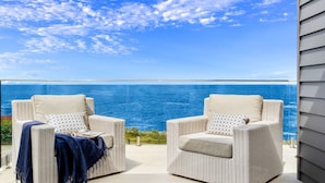 Deux fauteuils en osier avec des coussins, sur un balcon extérieur donnant sur l’océan.