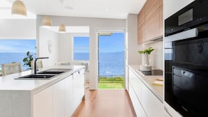 Une cuisine moderne avec vue sur la mer, dotée de meubles blancs, d’une cuisinière noire et d’une grande fenêtre.