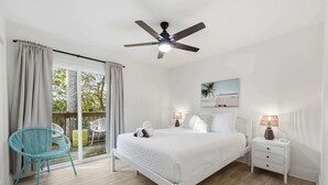 Ein Schlafzimmer mit Bett, Nachttisch, Sessel, Deckenventilator und Fenster mit Vorhängen.