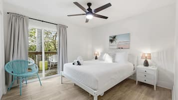 Quarto com cama, mesa de cabeceira, cadeira, ventilador de teto e janela com cortinas.