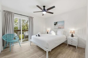 A bedroom with a bed, a nightstand, a chair, a ceiling fan, and a window with curtains. - Toes in the Sand Retreat II (Jacksonville Beach)