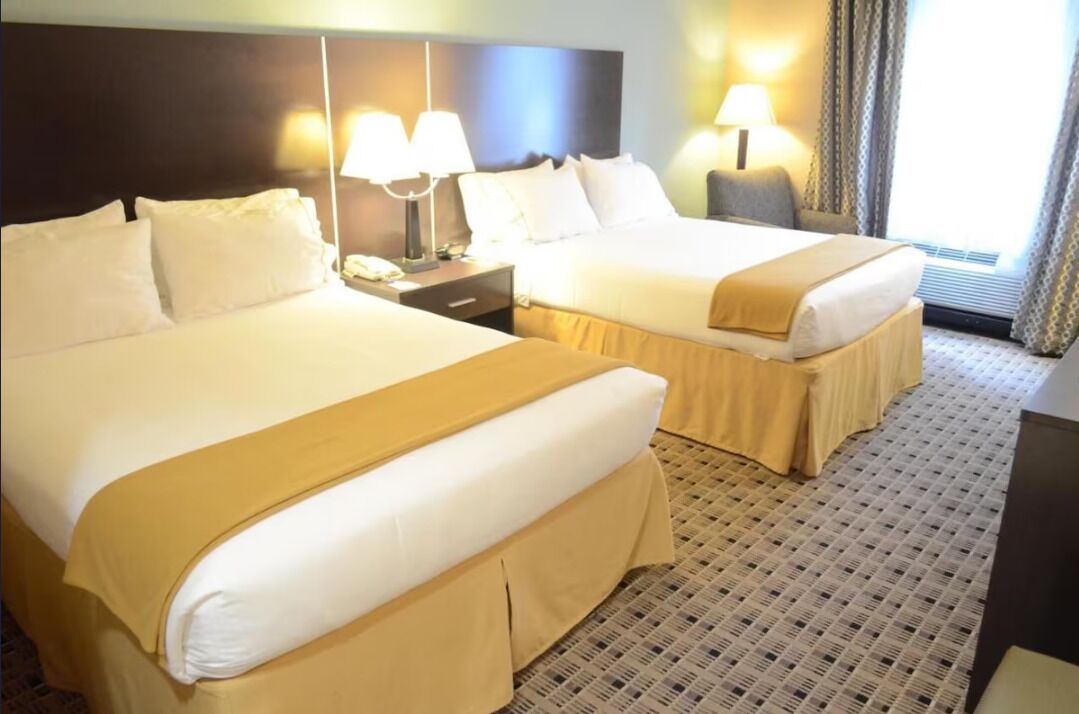 Una habitación de hotel con dos camas, una mesita de noche con lámpara y una ventana con cortinas.