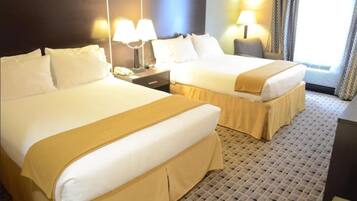 Una habitación de hotel con dos camas, una mesita de noche con lámpara y una ventana con cortinas.