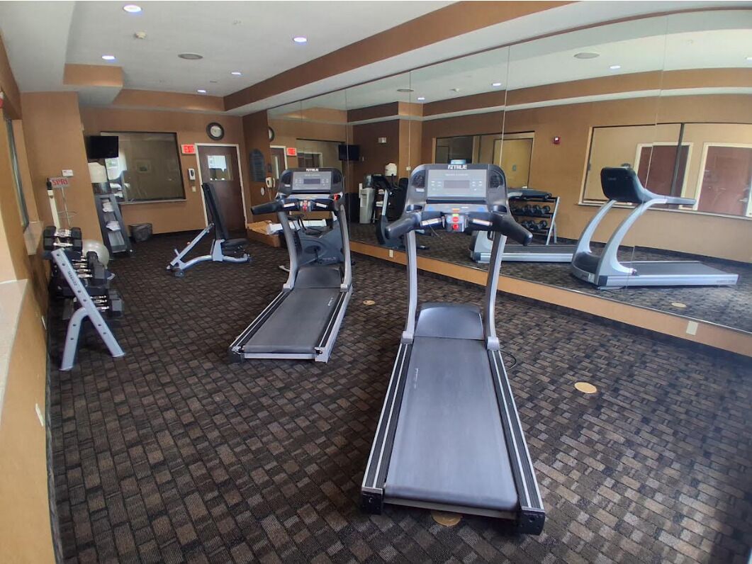 Un gimnasio con cintas de correr, máquinas de pesas y un espejo grande.