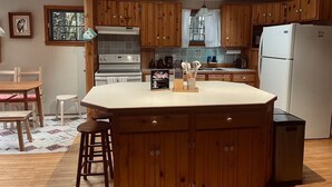 Une cuisine avec des meubles de rangement en bois, un îlot central, une cuisinière et un réfrigérateur.
