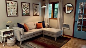 Un salon comprenant un canapé d’angle, une petite table d’appoint avec une plante, un tapis et des reproductions botaniques encadrées accrochées au mur.