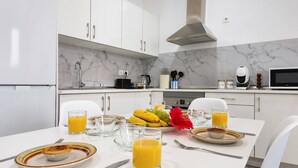 Een moderne keuken met witte kastjes, een marmeren spatwand en een eettafel gedekt met ontbijtartikelen, waaronder een muffin, sap en fruit.