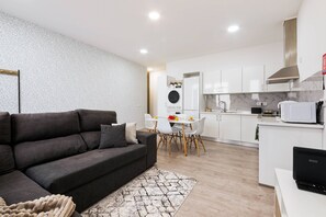 Ein modernes Wohnzimmer mit einem dunkelgrauen Sofa, einem gemusterten Teppich und einem Essbereich mit weißem Tisch und Stühlen.