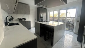 Eine moderne Küche mit einer großen Kochinsel, integrierten Geräten und einer Glastür zum Balkon.