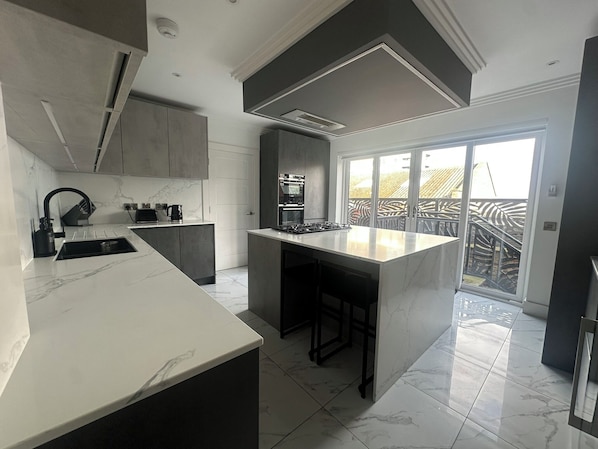 A modern kitchen with a large island, built-in appliances, and a sliding glass door leading to a balcony.
