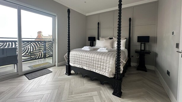 Ein Bett mit Baldachin, eine gesteppte Bettdecke, ein Flachbildfernseher auf einem Standfuß und eine Glastür zum Balkon.