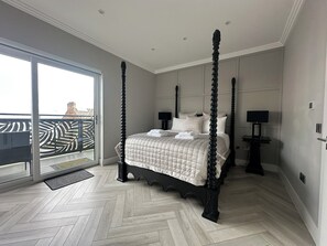 A four-poster bed with a quilted bedspread, a flat-screen TV on a stand, and a sliding glass door leading to a balcony.