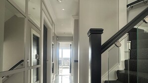 Ein moderner Flur mit Glastür zum Balkon, einer Treppe mit schwarzen Geländern und einem Marmorboden.
