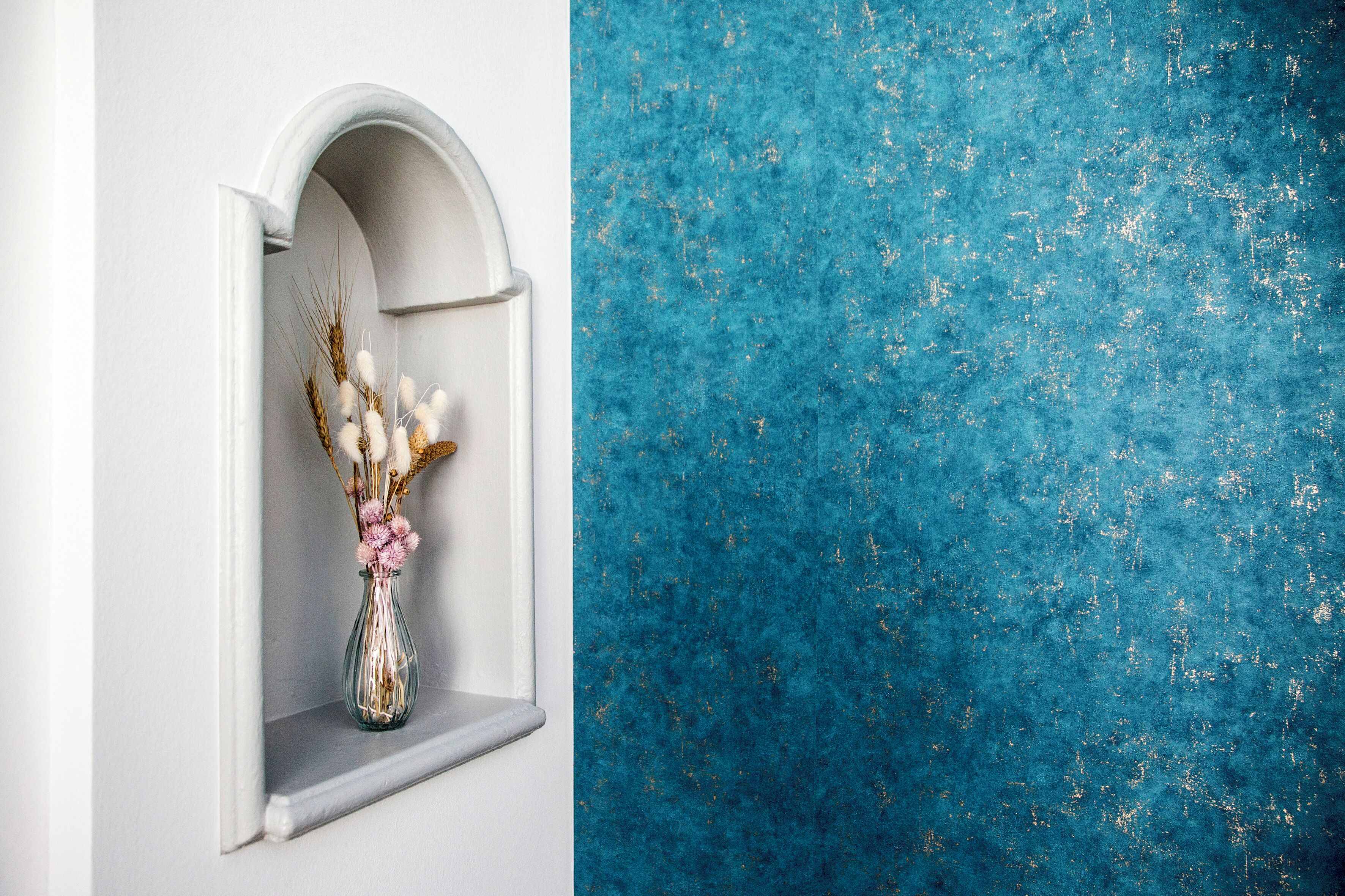 Una ventana arqueada blanca con un florero de flores secas.