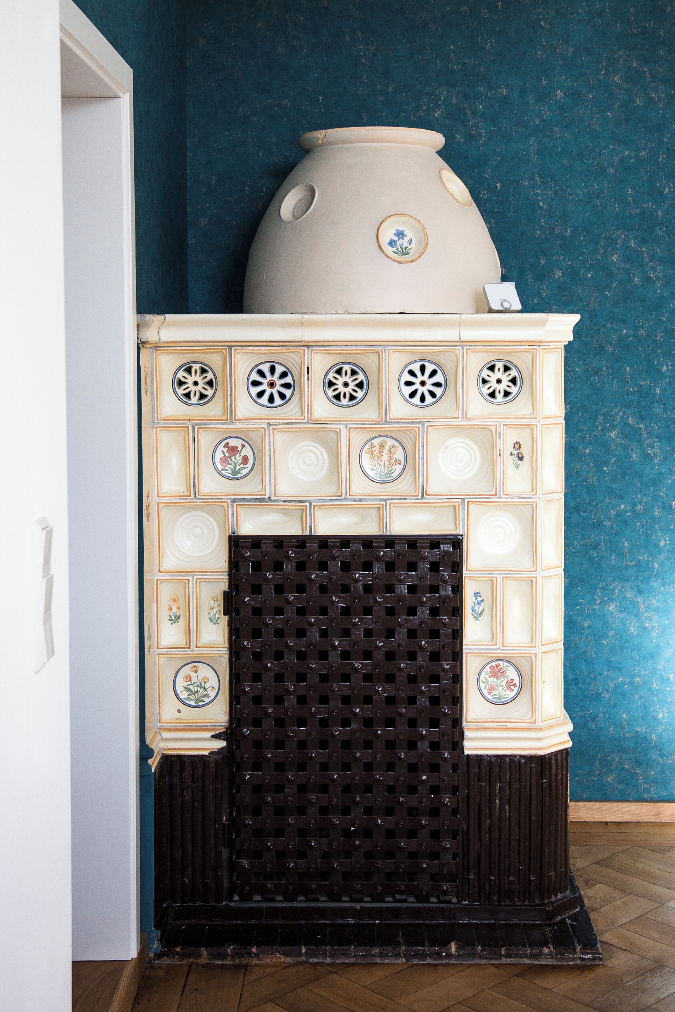 Une cheminée agrémentée d’un manteau décoratif en faïence et surmontée d’un grand vase.