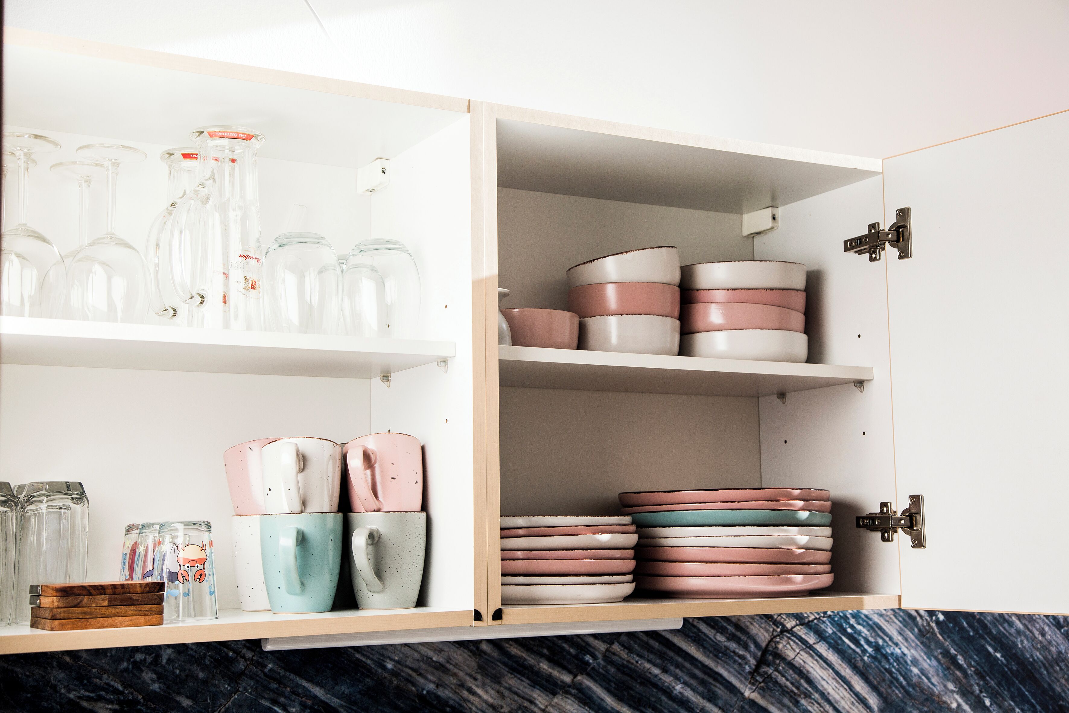 A kitchen with open cabinets displaying glassware, ceramic mugs, and plates.