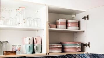 A kitchen with open cabinets displaying glassware, ceramic mugs, and plates.