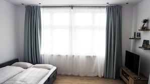 Un dormitori amb un llit, una televisió i una finestra amb cortines.