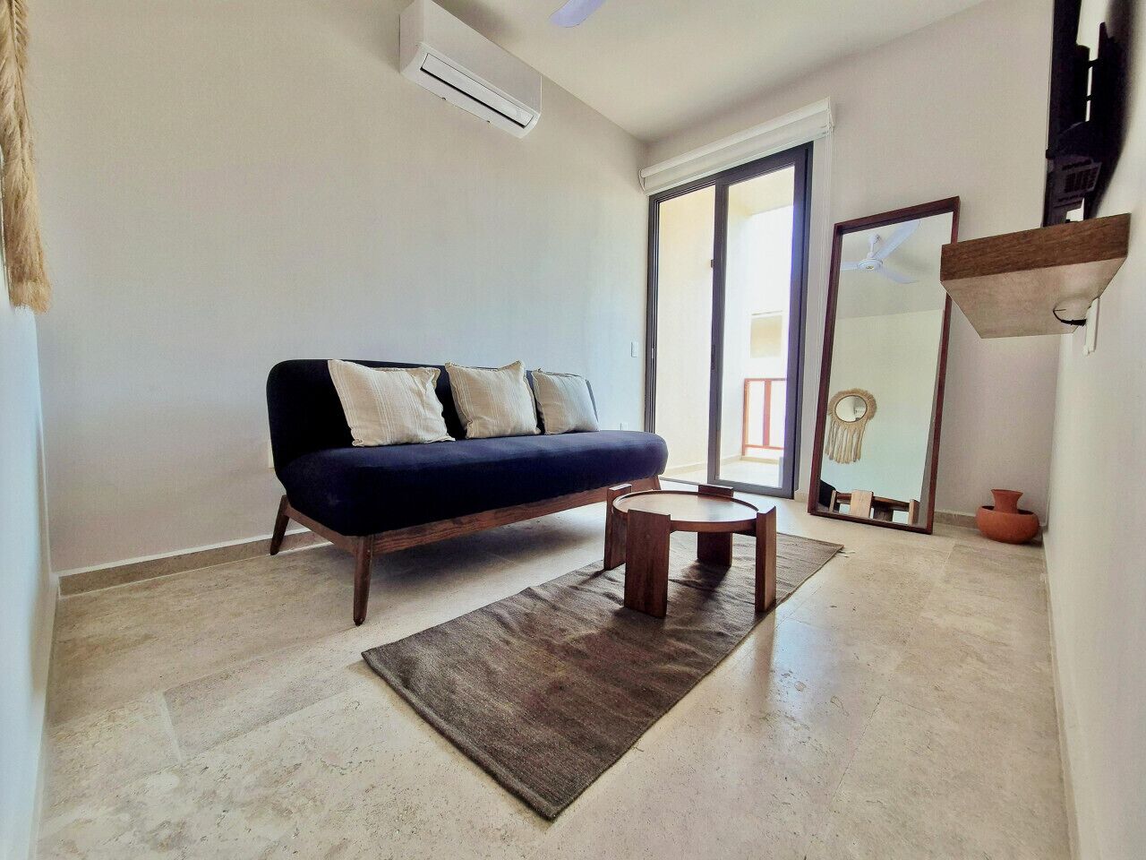 A living room with a dark blue sofa, a round wooden coffee table, and a large mirror on the wall.
