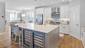 Une cuisine moderne avec des meubles blancs, un grand îlot central doté de tabourets, des appareils en acier inoxydable et un éclairage encastré au plafond.