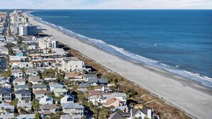 Une zone résidentielle côtière avec des propriétés donnant sur la plage, une jetée et un ciel dégagé.