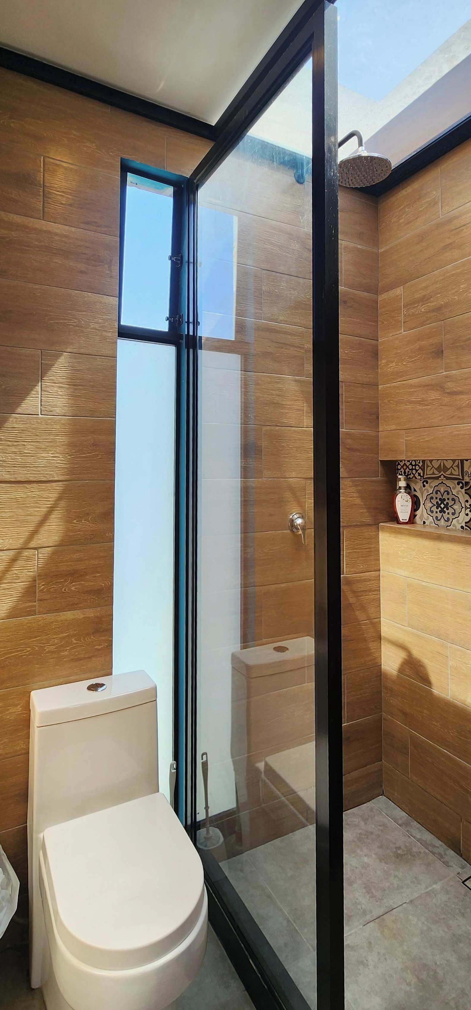 A modern bathroom with a glass shower enclosure, wooden walls, and a white toilet.