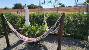 A hammock between two wooden posts in a garden area with green bushes and a brown fence in the background.