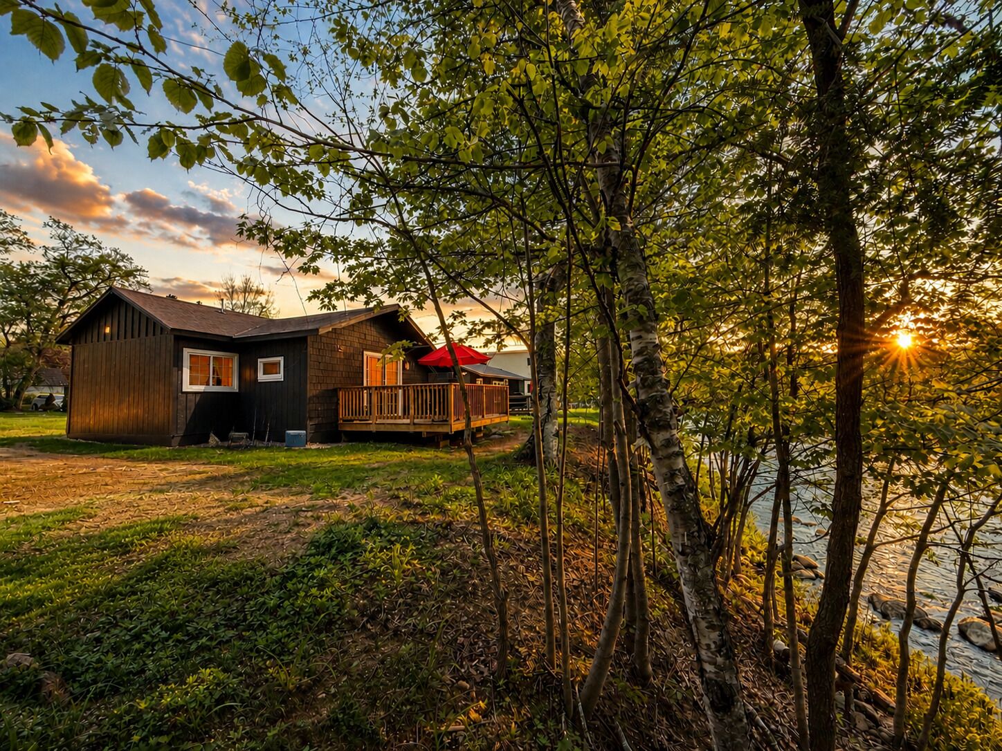Una cabaña con terraza y vistas a un lago al atardecer.