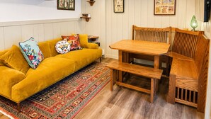 A cozy living room with a yellow sofa, wooden dining table, and patterned rug. - Riverside Cottage • Private Beach • Mountain Views (Bartlett)