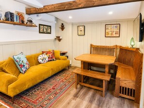 Una sala de estar acogedora con un sofá amarillo, una mesa de comedor de madera y un tapete estampado.