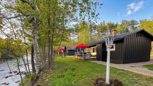 A cabin with a deck, a red umbrella, and a river. - Riverside Cottage • Private Beach • Mountain Views (Bartlett)