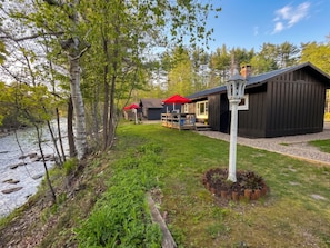 Une cabane avec une terrasse, un parasol rouge et une rivière.