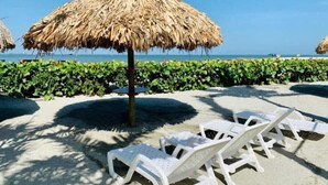 Une plage avec des parasols en chaume et des chaises longues blanches.