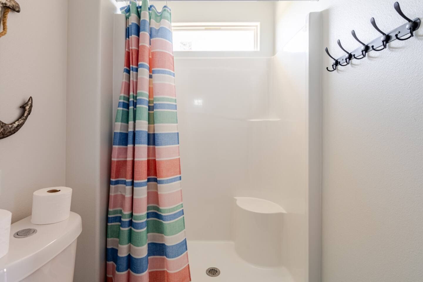Kylpyhuone, jossa on suihkuverho, wc-paperia ja seinälle kiinnitetty naulakko.