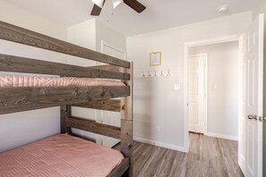 A bedroom with two bunk beds, a door, a coat rack, and a ceiling fan. - Sunset Bellini - Hot Tub, Golf Cart, Dog Friendly! (Bolivar Peninsula)